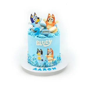 Bluey birthday cake with blue frosting, character toppers, macarons, number two topper, sprinkles, and name detail.