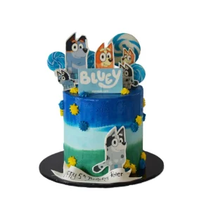 Bluey-themed birthday cake decorated with character cutouts, swirled lollipops, and floral accents, featuring a “Happy 5th Birthday Peter” message and a “Bluey For Real Life” topper.
