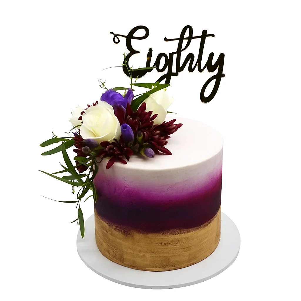 Elegant 80th birthday cake by Amarantos Cakes featuring a smooth gold-to-purple gradient buttercream, fresh white roses, purple and dark red blooms, green foliage, and a cursive “Eighty” topper.