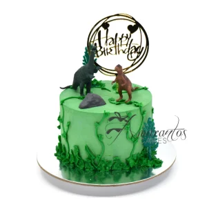 Dinosaur-themed birthday cake by Amarantos Cakes featuring green buttercream, icing vines and foliage, plastic dinosaur figurines, a grey rock decoration, and a stylised “Happy Birthday” topper with heart accents.