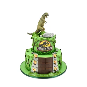 Jurassic Park-themed two-tier birthday cake with fondant dinosaur, jungle leaves, logo, entrance gates, and name Alessandre.