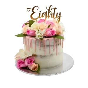 Semi-naked 80th birthday cake by Amarantos Cakes featuring white icing, pink drip glaze, fresh roses in shades of pink, peach, and white, and a cursive gold “Eighty” topper.