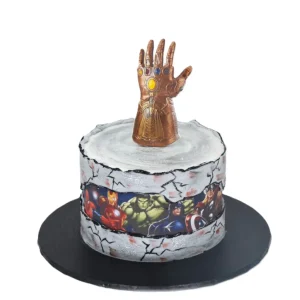Marvel Avengers-themed birthday cake by Amarantos Cakes featuring cracked stone-textured sides, a printed image strip of Avengers characters, and a detailed Infinity Gauntlet topper with coloured stones.
