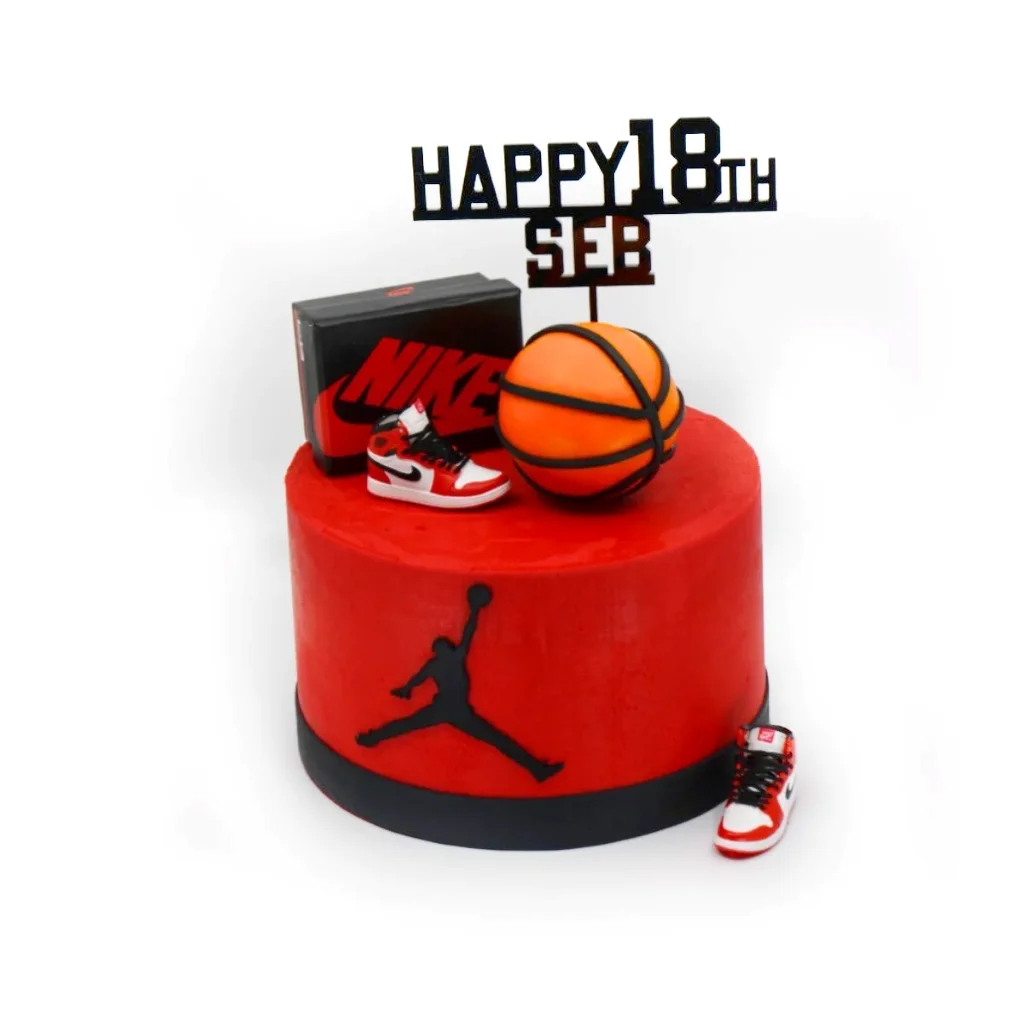 Basketball-themed birthday cake with red and black buttercream, featuring Air Jordan logo, Nike shoebox, basketball, and miniature sneakers.