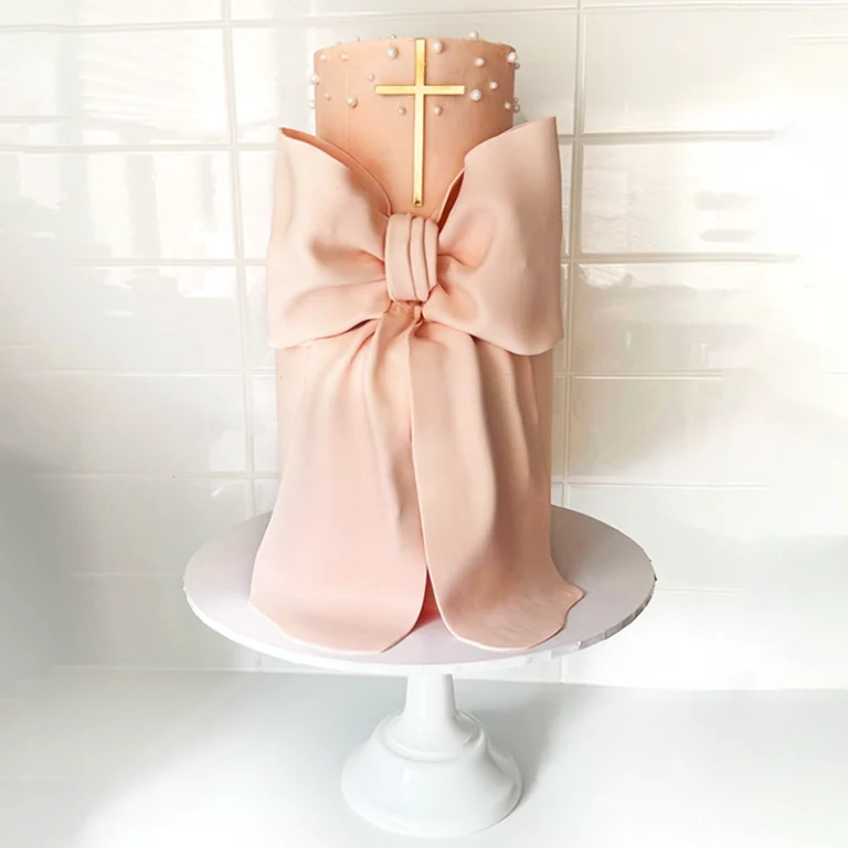 Pink Christening cake with a bow and golden gross sitting in a cake stand.