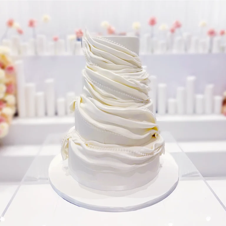 A stunning white wedding cake with pearls sitting as the centerpiece.