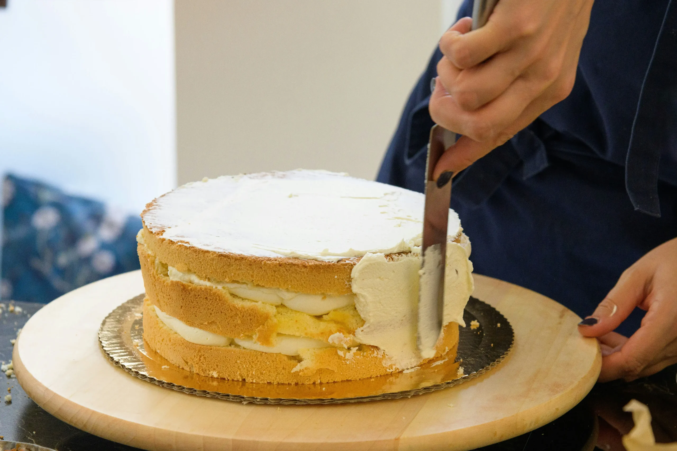Women spreading buttercream on a cake she is making.
